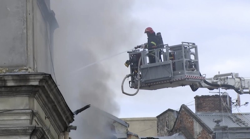 Warga melihat petugas pemadam kebakaran yang bekerja di lokasi bangunan yang terkena serangan pesawat tak berawak Rusia, di tengah serangan Rusia terhadap Ukraina, di pusat kota Lviv, Ukraina, 24 Maret 2026. (REUTERS/Stringer)