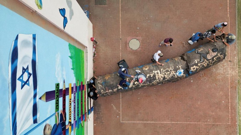 Seorang gadis berpose untuk foto di samping sisa-sisa rudal yang tertancap di tanah yang ditemukan di desa Kifl Haris, dekat Nablus di Tepi Barat yang diduduki Israel, 24 Maret 2026. (REUTERS/Mohammed Torokman/File Photo)