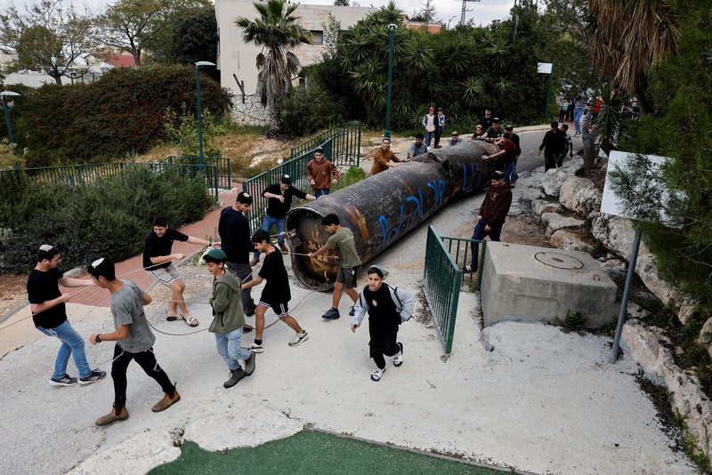 Seorang gadis berpose untuk foto di samping sisa-sisa rudal yang tertancap di tanah yang ditemukan di desa Kifl Haris, dekat Nablus di Tepi Barat yang diduduki Israel, 24 Maret 2026. (REUTERS/Mohammed Torokman/File Photo)
