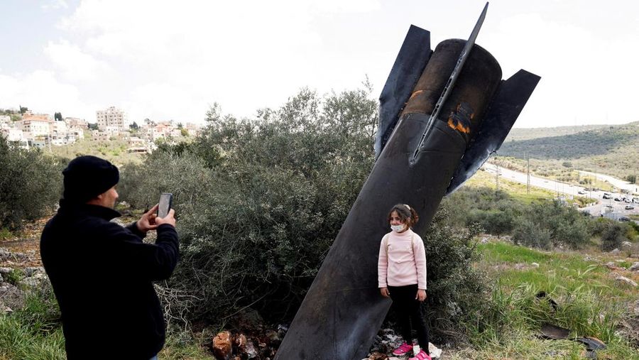 Seorang gadis berpose untuk foto di samping sisa-sisa rudal yang tertancap di tanah yang ditemukan di desa Kifl Haris, dekat Nablus di Tepi Barat yang diduduki Israel, 24 Maret 2026. (REUTERS/Mohammed Torokman/File Photo)