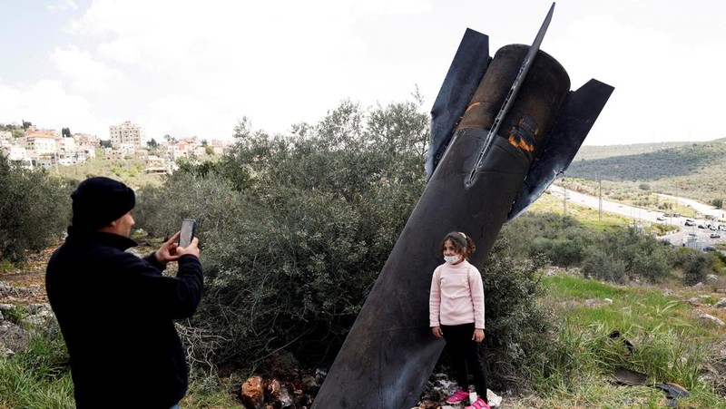 Seorang gadis berpose untuk foto di samping sisa-sisa rudal yang tertancap di tanah yang ditemukan di desa Kifl Haris, dekat Nablus di Tepi Barat yang diduduki Israel, 24 Maret 2026. (REUTERS/Mohammed Torokman/File Photo)