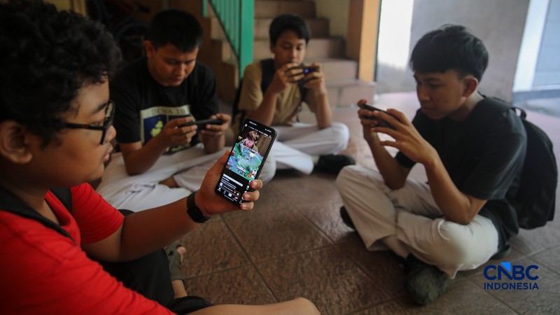 Sejumlah anak memainkan ponsel mereka sesuai pulang sekolah di Jakarta, Senin (30/3/2026). Pemerintah resmi melarang anak di bawah usia 16 tahun menggunakan media sosial mulai 28 Maret 2026 berdasarkan Peraturan Menteri Komunikasi dan Digital Nomor 9 Tahun 2026, yang merupakan turunan dari PP Tunas. (CNBC Indonesia/Faisal Rahman)