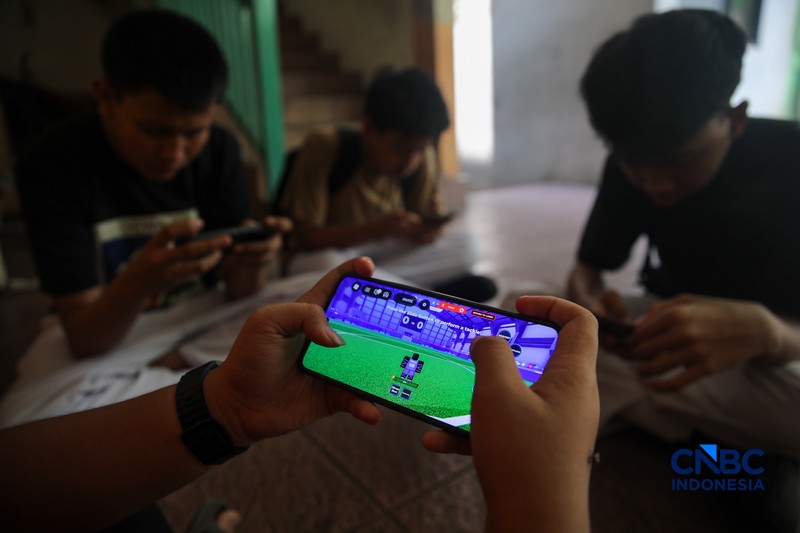 Sejumlah anak memainkan ponsel mereka sesuai pulang sekolah di Jakarta, Senin (30/3/2026). Pemerintah resmi melarang anak di bawah usia 16 tahun menggunakan media sosial mulai 28 Maret 2026 berdasarkan Peraturan Menteri Komunikasi dan Digital Nomor 9 Tahun 2026, yang merupakan turunan dari PP Tunas. (CNBC Indonesia/Faisal Rahman)