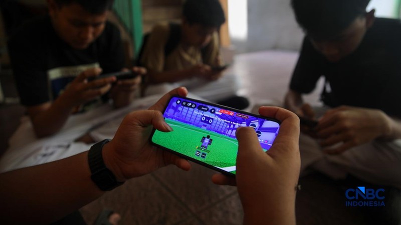 Sejumlah anak memainkan ponsel mereka sesuai pulang sekolah di Jakarta, Senin (30/3/2026). Pemerintah resmi melarang anak di bawah usia 16 tahun menggunakan media sosial mulai 28 Maret 2026 berdasarkan Peraturan Menteri Komunikasi dan Digital Nomor 9 Tahun 2026, yang merupakan turunan dari PP Tunas. (CNBC Indonesia/Faisal Rahman)