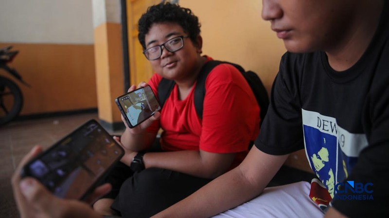 Sejumlah anak memainkan ponsel mereka sesuai pulang sekolah di Jakarta, Senin (30/3/2026). Pemerintah resmi melarang anak di bawah usia 16 tahun menggunakan media sosial mulai 28 Maret 2026 berdasarkan Peraturan Menteri Komunikasi dan Digital Nomor 9 Tahun 2026, yang merupakan turunan dari PP Tunas. (CNBC Indonesia/Faisal Rahman)