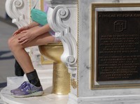 Seseorang duduk di atas patung yang menampilkan toilet emas besar, berjudul "Singgasana yang Layak untuk Seorang Raja," yang dipajang di dekat Monumen Lincoln di National Mall di Washington, D.C., AS, 30 Maret 2026. (REUTERS/Evelyn Hockstein)