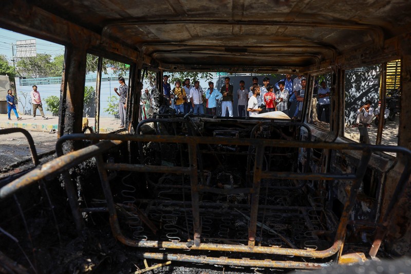 Seorang wanita berjalan melewati deretan mobil hangus yang berjejer di luar Maruti Suzuki Car Center, yang rusak selama protes pekerja, setelah para pekerja pabrik menuntut kenaikan upah, di tengah melonjaknya biaya hidup akibat gangguan yang disebabkan oleh konflik AS-Israel dengan Iran, di Noida, kota pusat industri India di negara bagian Uttar Pradesh, India, 13 April 2026. (REUTERS/Anushree Fadnavis)