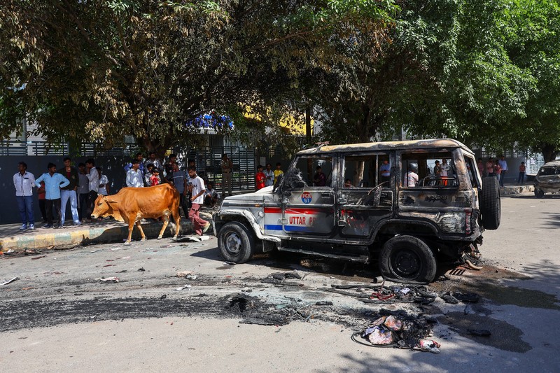 Seorang wanita berjalan melewati deretan mobil hangus yang berjejer di luar Maruti Suzuki Car Center, yang rusak selama protes pekerja, setelah para pekerja pabrik menuntut kenaikan upah, di tengah melonjaknya biaya hidup akibat gangguan yang disebabkan oleh konflik AS-Israel dengan Iran, di Noida, kota pusat industri India di negara bagian Uttar Pradesh, India, 13 April 2026. (REUTERS/Anushree Fadnavis)
