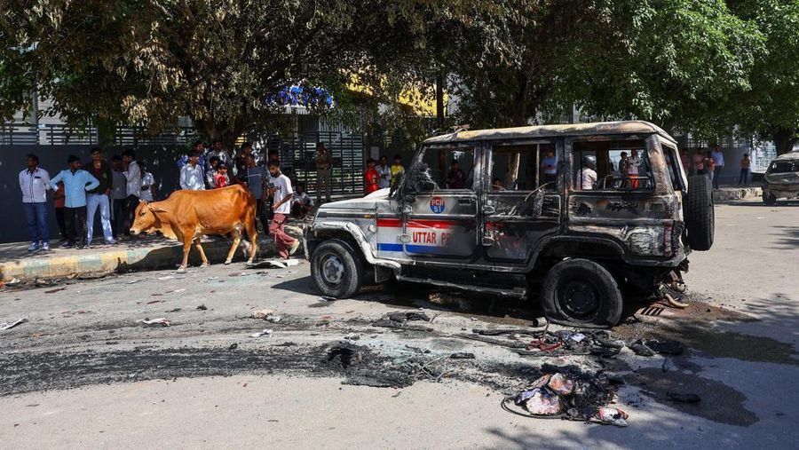 Seorang wanita berjalan melewati deretan mobil hangus yang berjejer di luar Maruti Suzuki Car Center, yang rusak selama protes pekerja, setelah para pekerja pabrik menuntut kenaikan upah, di tengah melonjaknya biaya hidup akibat gangguan yang disebabkan oleh konflik AS-Israel dengan Iran, di Noida, kota pusat industri India di negara bagian Uttar Pradesh, India, 13 April 2026. (REUTERS/Anushree Fadnavis)