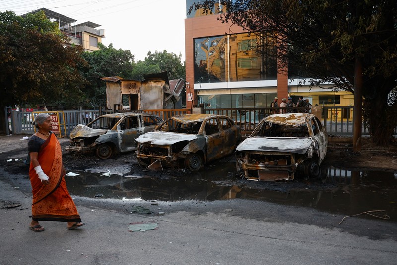 Seorang wanita berjalan melewati deretan mobil hangus yang berjejer di luar Maruti Suzuki Car Center, yang rusak selama protes pekerja, setelah para pekerja pabrik menuntut kenaikan upah, di tengah melonjaknya biaya hidup akibat gangguan yang disebabkan oleh konflik AS-Israel dengan Iran, di Noida, kota pusat industri India di negara bagian Uttar Pradesh, India, 13 April 2026. (REUTERS/Anushree Fadnavis)