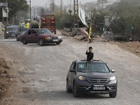 Seorang anak laki-laki melambaikan bendera dari dalam kendaraan saat para pengungsi kembali ke rumah mereka menyeberangi jembatan yang menghubungkan Lebanon selatan dengan bagian negara lainnya, yang sebelumnya dihantam serangan Israel, setelah genca