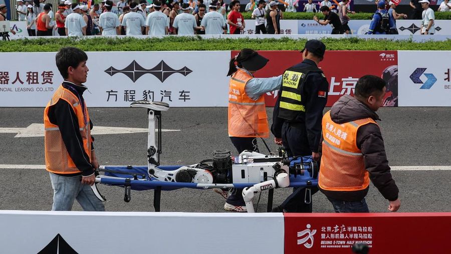 Para staf membawa robot humanoid yang jatuh setelah garis finis pada ajang Beijing E-Town Half Marathon dan Humanoid Robot Half Marathon kedua di Beijing, China, 19 April 2026.