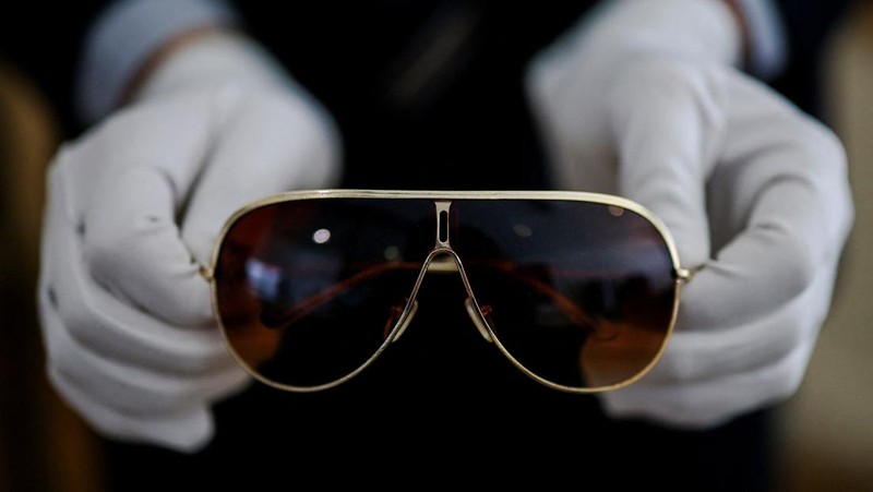 Arthur Perault, kepala Departemen Budaya Pop dan Memorabilia Aguttes, memegang kacamata hitam bergaya pilot milik Michael Jackson, yang dikaitkan dengan periode Victory Tour (1984) sebelum lelang koleksi yang didedikasikan untuk Michael Jackson di rumah lelang Aguttes di Neuilly-sur-Seine, dekat Paris, Prancis, 23 April 2026.