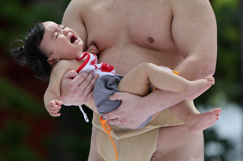 Pegulat sumo amatir menggendong bayi selama 'Nakizumo' atau kontes sumo bayi menangis di kuil Sensoji di Tokyo, Jepang, Sabtu (25/4/2026). (REUTERS/Issei Kato)