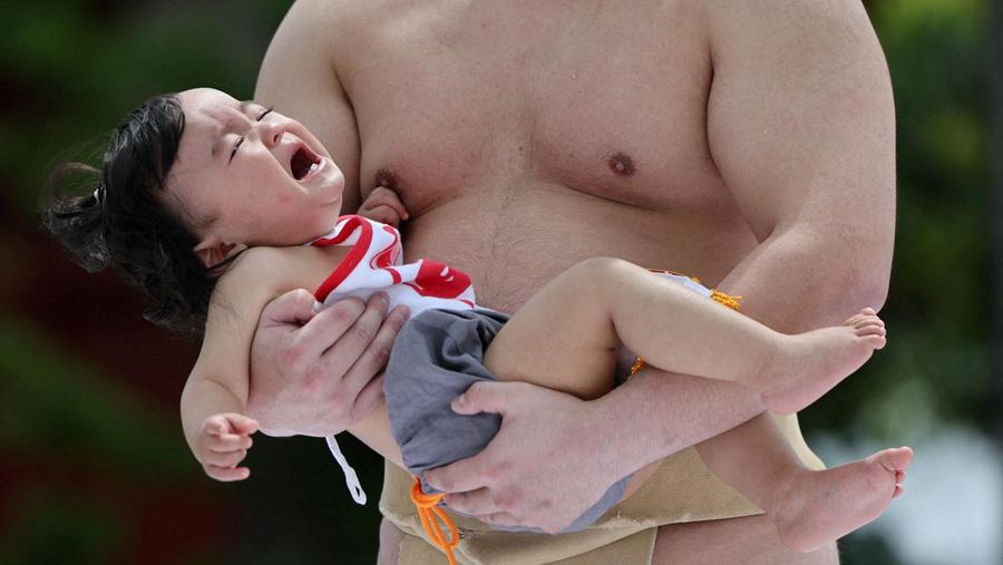 Pegulat sumo amatir menggendong bayi selama 'Nakizumo' atau kontes sumo bayi menangis di kuil Sensoji di Tokyo, Jepang, Sabtu (25/4/2026). (REUTERS/Issei Kato)