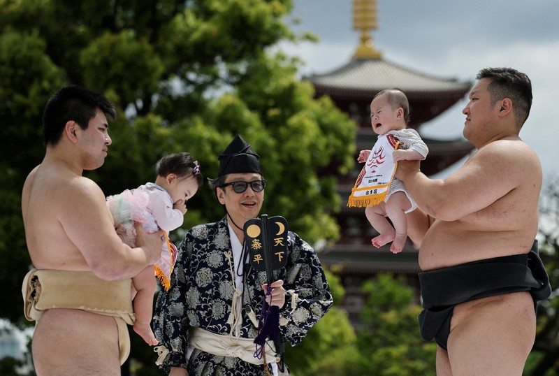 Pegulat sumo amatir menggendong bayi selama 'Nakizumo' atau kontes sumo bayi menangis di kuil Sensoji di Tokyo, Jepang, Sabtu (25/4/2026). (REUTERS/Issei Kato)