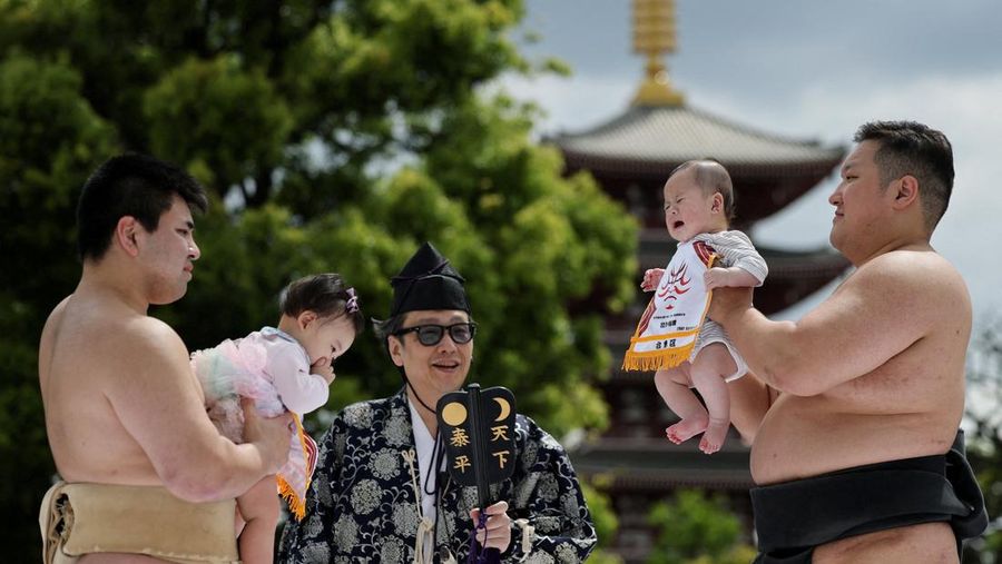 Pegulat sumo amatir menggendong bayi selama 'Nakizumo' atau kontes sumo bayi menangis di kuil Sensoji di Tokyo, Jepang, Sabtu (25/4/2026). (REUTERS/Issei Kato)