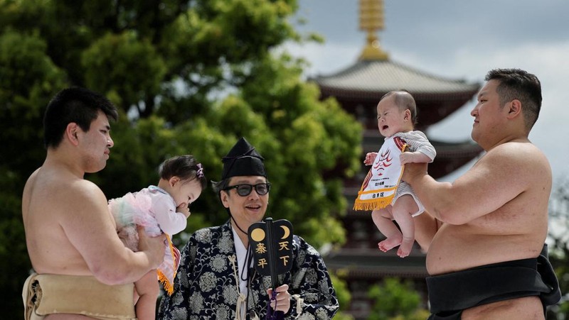 Pegulat sumo amatir menggendong bayi selama 'Nakizumo' atau kontes sumo bayi menangis di kuil Sensoji di Tokyo, Jepang, Sabtu (25/4/2026). (REUTERS/Issei Kato)