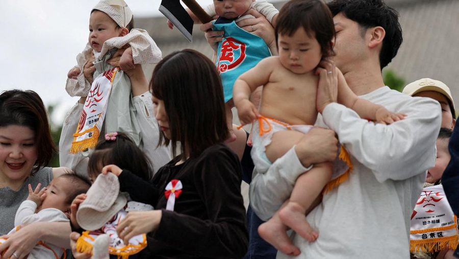 Pegulat sumo amatir menggendong bayi selama 'Nakizumo' atau kontes sumo bayi menangis di kuil Sensoji di Tokyo, Jepang, Sabtu (25/4/2026). (REUTERS/Issei Kato)