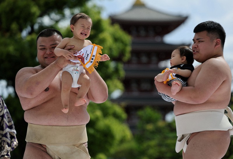 Pegulat sumo amatir menggendong bayi selama 'Nakizumo' atau kontes sumo bayi menangis di kuil Sensoji di Tokyo, Jepang, Sabtu (25/4/2026). (REUTERS/Issei Kato)