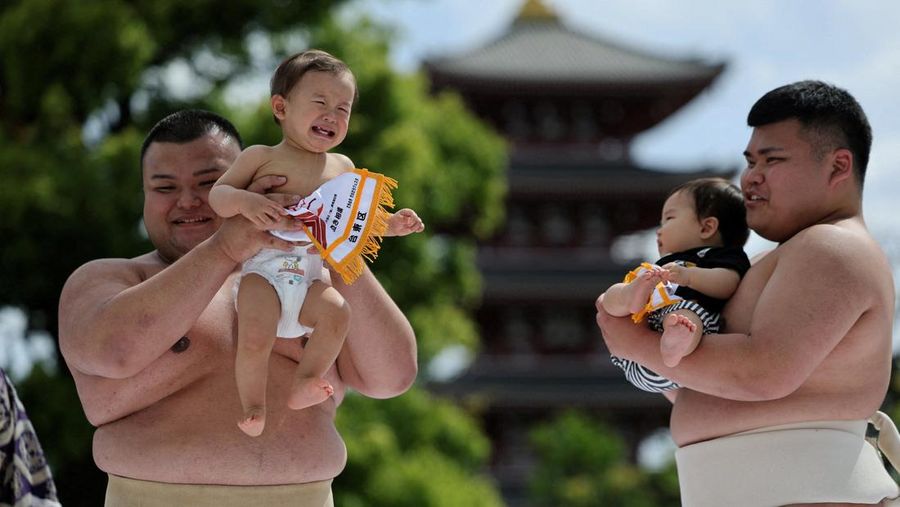 Pegulat sumo amatir menggendong bayi selama 'Nakizumo' atau kontes sumo bayi menangis di kuil Sensoji di Tokyo, Jepang, Sabtu (25/4/2026). (REUTERS/Issei Kato)