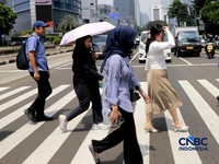 Warga berjalan dengan menutup kepala untuk berlindung dari terik matahari di Sudirman, Jakarta, Rabu (29/4/2026). (CNBC Indonesia/Muhammad Sabki)