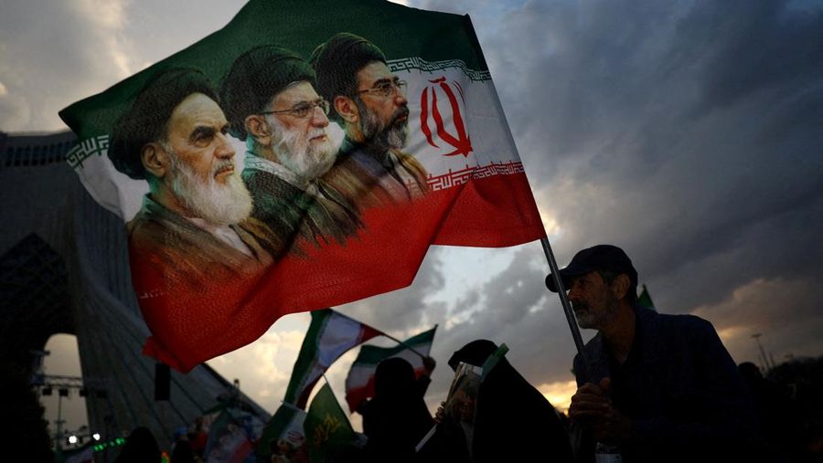FILE PHOTO: A man holds a flag with a picture of late leader of the Islamic Revolution Ayatollah Ruhollah Khomeini, late Supreme Leader of Iran Ayatollah Ali Khamenei and Iran's new Supreme Leader Mojtaba Khamenei, during a rally in Tehran, Iran, Apr