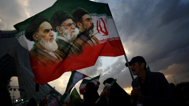 FILE PHOTO: A man holds a flag with a picture of late leader of the Islamic Revolution Ayatollah Ruhollah Khomeini, late Supreme Leader of Iran Ayatollah Ali Khamenei and Iran's new Supreme Leader Mojtaba Khamenei, during a rally in Tehran, Iran, Apr
