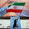 A woman waves an Iranian flag in front of an anti-US billboard referring to US President Donald Trump and the Strait of Hormuz at Valiasr Square in Tehran on May 5, 2026. Iran's chief negotiator in talks with the United States warned on May 5 that hi