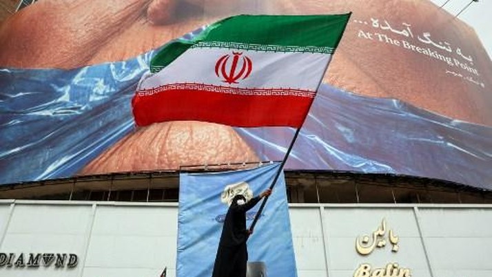 A woman waves an Iranian flag in front of an anti-US billboard referring to US President Donald Trump and the Strait of Hormuz at Valiasr Square in Tehran on May 5, 2026. Iran's chief negotiator in talks with the United States warned on May 5 that hi
