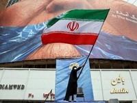 A woman waves an Iranian flag in front of an anti-US billboard referring to US President Donald Trump and the Strait of Hormuz at Valiasr Square in Tehran on May 5, 2026. Iran's chief negotiator in talks with the United States warned on May 5 that hi