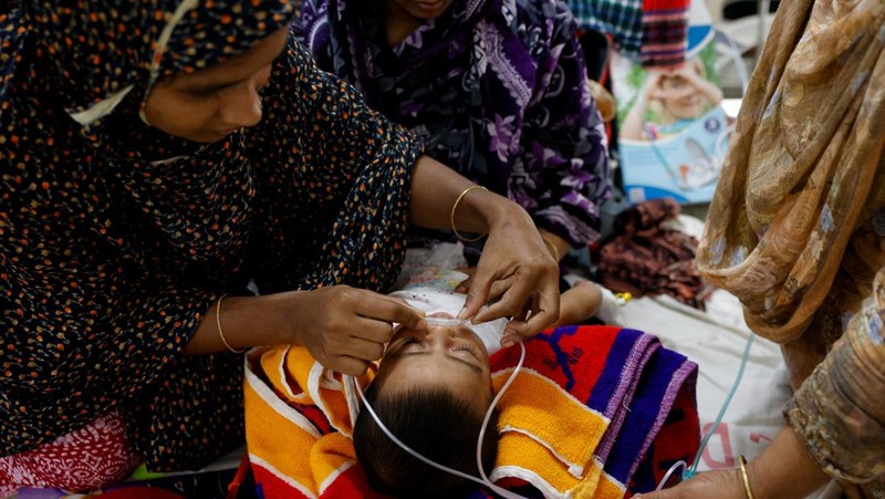 Seorang wanita menyesuaikan selang untuk memastikan pasokan oksigen tambahan kepada seorang anak yang terinfeksi campak yang sedang dirawat di Rumah Sakit DNCC, menyusul wabah yang terjadi di seluruh negeri, di Dhaka, Bangladesh, 6 Mei 2026.