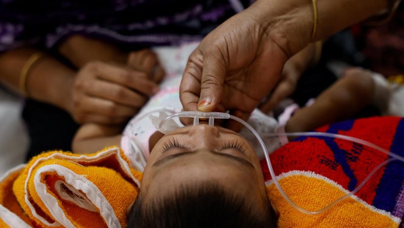 Seorang wanita menyesuaikan selang untuk memastikan pasokan oksigen tambahan kepada seorang anak yang terinfeksi campak yang sedang dirawat di Rumah Sakit DNCC, menyusul wabah yang terjadi di seluruh negeri, di Dhaka, Bangladesh, 6 Mei 2026.