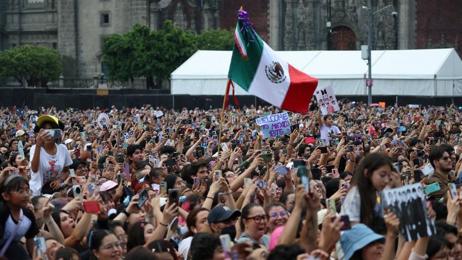 A Mexican flag waves as fans of South Korean Kpop boy band BTS, known as ARMY, look on on the day members of the band meet with Mexico's President Claudia Sheinbaum at the National Palace ahead of a series of concerts on the BTS World Tour