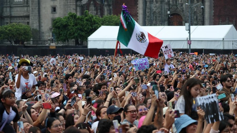A Mexican flag waves as fans of South Korean Kpop boy band BTS, known as ARMY, look on on the day members of the band meet with Mexico's President Claudia Sheinbaum at the National Palace ahead of a series of concerts on the BTS World Tour