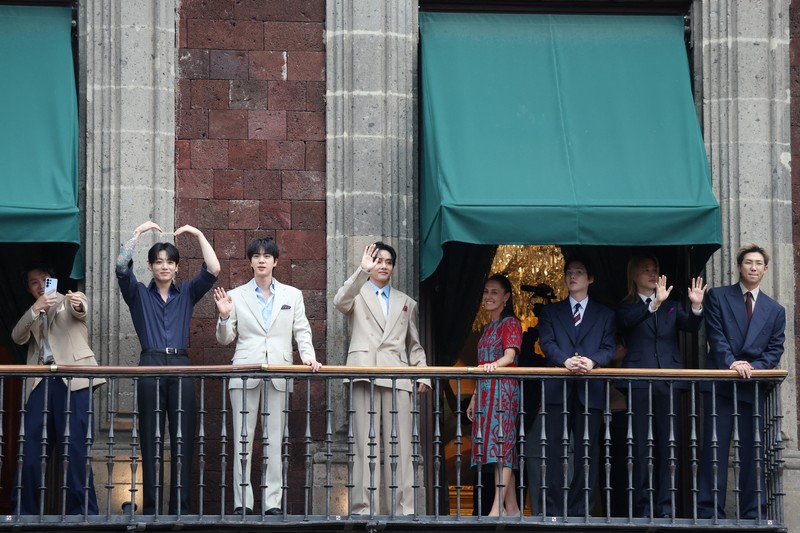 Mexico's President Claudia Sheinbaum and members of South Korean Kpop boy band BTS react as they stand on a balcony of the National Palace ahead of a series of concerts on the BTS World Tour