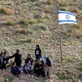 Palestinian school children stand near an Israeli flag as they returns home walking past fencing and razor wire recently erected by Israeli settlers to block the local shortcut route used to reach their school, forcing them to take a detour along the