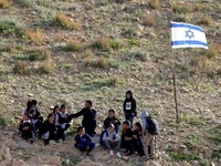 Palestinian school children stand near an Israeli flag as they returns home walking past fencing and razor wire recently erected by Israeli settlers to block the local shortcut route used to reach their school, forcing them to take a detour along the