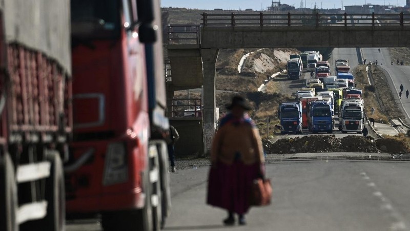 Seorang wanita berjalan di antara truk-truk yang terhenti selama berhari-hari karena para pengunjuk rasa memblokir jalan raya utama, menuntut pengunduran diri Presiden Rodrigo Paz di tengah krisis ekonomi dan bahan bakar yang sedang berlangsung, di Apacheta, Bolivia, 13 Mei 2026.