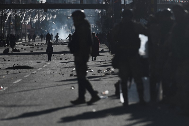 Seorang petugas polisi militer berjalan sementara seorang anak berdiri di antara bebatuan yang berserakan di jalan saat para pengunjuk rasa berdemonstrasi menentang pemerintahan Presiden Rodrigo Paz di tengah krisis ekonomi dan bahan bakar yang sedang berlangsung, di El Alto, Bolivia, 16 Mei 2026. (REUTERS/Claudia Morales)
