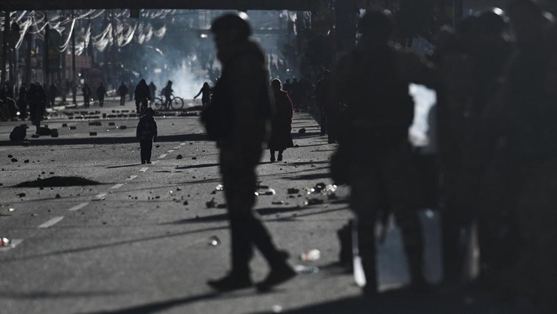 Seorang petugas polisi militer berjalan sementara seorang anak berdiri di antara bebatuan yang berserakan di jalan saat para pengunjuk rasa berdemonstrasi menentang pemerintahan Presiden Rodrigo Paz di tengah krisis ekonomi dan bahan bakar yang sedan