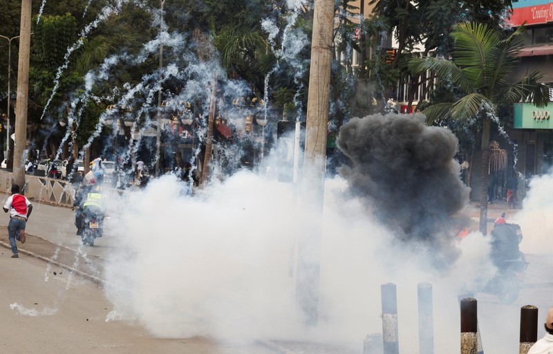 Petugas polisi anti huru hara berlari untuk membubarkan demonstran melewati mayat seorang pria yang tewas selama pemogokan operator transportasi umum yang dipicu oleh kenaikan biaya bahan bakar terkait dengan tekanan pasokan global, di kota Nakuru, Lembah Rift, Kenya, 18 Mei 2026. (REUTERS/Suleiman Mbatiah)