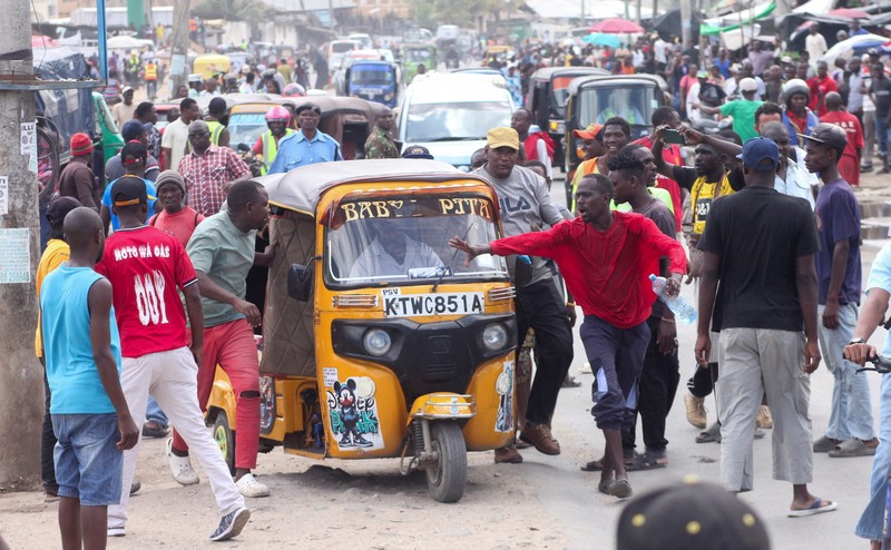 Petugas polisi anti huru hara berlari untuk membubarkan demonstran melewati mayat seorang pria yang tewas selama pemogokan operator transportasi umum yang dipicu oleh kenaikan biaya bahan bakar terkait dengan tekanan pasokan global, di kota Nakuru, Lembah Rift, Kenya, 18 Mei 2026. (REUTERS/Suleiman Mbatiah)