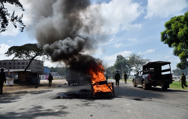 Petugas polisi anti huru hara berlari untuk membubarkan demonstran melewati mayat seorang pria yang tewas selama pemogokan operator transportasi umum yang dipicu oleh kenaikan biaya bahan bakar terkait dengan tekanan pasokan global, di kota Nakuru, Lembah Rift, Kenya, 18 Mei 2026. (REUTERS/Suleiman Mbatiah)