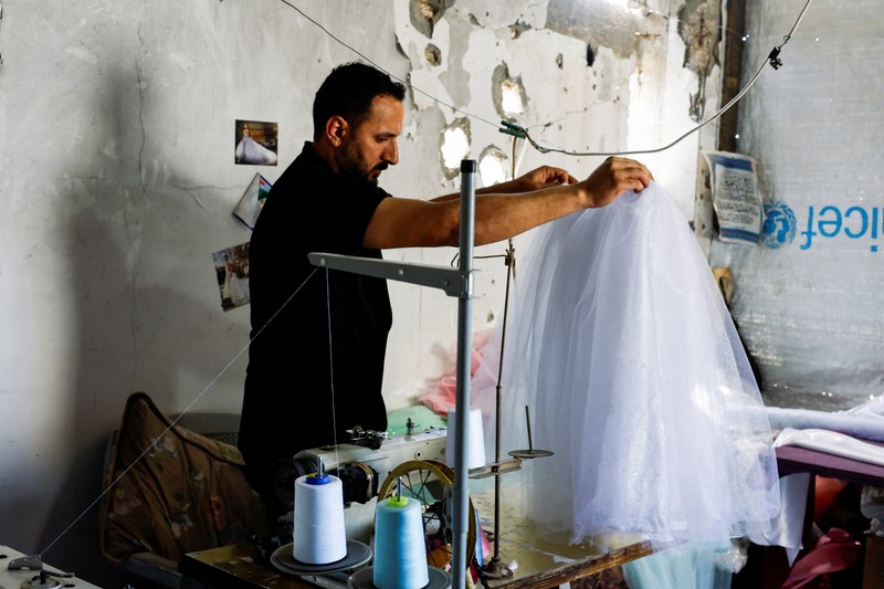 Seorang wanita Palestina melihat gaun pengantin yang dipajang di luar sebuah toko di samping tumpukan puing, saat para pengantin wanita di Gaza beralih ke gaun bekas di tengah kenaikan harga dan kekurangan yang disebabkan oleh perang, di Khan Younis di Jalur Gaza selatan, 9 Mei 2026. (REUTERS/Mahmoud Issa)