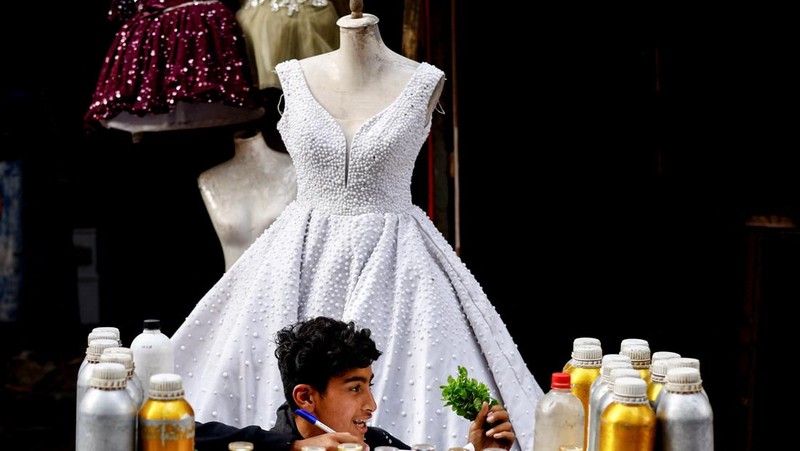 Seorang penjual parfum muda Palestina duduk di luar toko yang memajang gaun pengantin, karena para pengantin wanita di Gaza beralih ke gaun bekas di tengah kenaikan harga dan kekurangan yang disebabkan oleh perang, di Khan Younis di Jalur Gaza selatan, 9 Mei 2026.