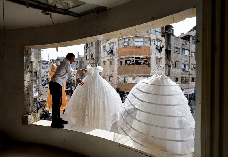 Seorang wanita Palestina melihat gaun pengantin yang dipajang di luar sebuah toko di samping tumpukan puing, saat para pengantin wanita di Gaza beralih ke gaun bekas di tengah kenaikan harga dan kekurangan yang disebabkan oleh perang, di Khan Younis di Jalur Gaza selatan, 9 Mei 2026. (REUTERS/Mahmoud Issa)