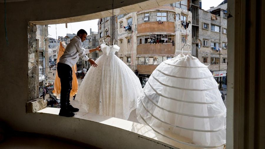 Seorang pria Palestina menggantung gaun pengantin di sebuah toko dengan dinding dan langit-langit yang rusak, karena para pengantin wanita di Gaza beralih ke gaun bekas di tengah kenaikan harga dan kekurangan yang disebabkan oleh perang, di Khan Younis di Jalur Gaza selatan, 9 Mei 2026.