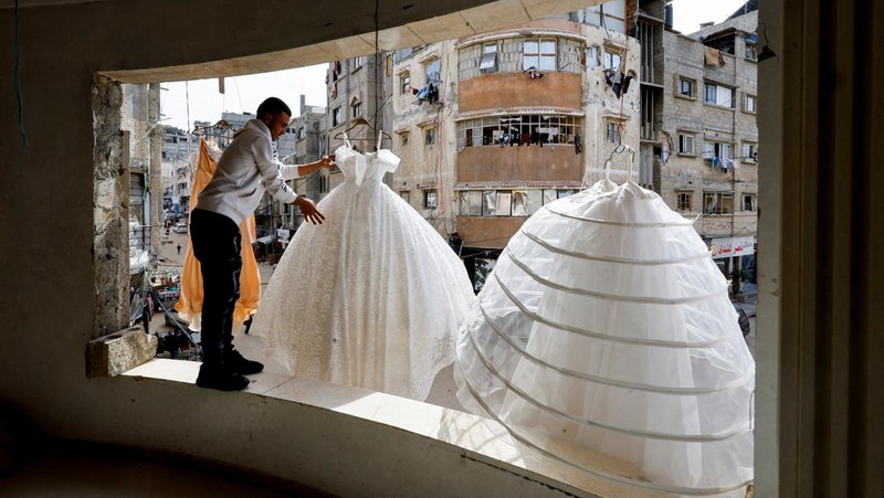 Seorang pria Palestina menggantung gaun pengantin di sebuah toko dengan dinding dan langit-langit yang rusak, karena para pengantin wanita di Gaza beralih ke gaun bekas di tengah kenaikan harga dan kekurangan yang disebabkan oleh perang, di Khan Younis di Jalur Gaza selatan, 9 Mei 2026.