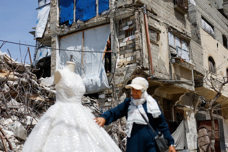 Seorang wanita Palestina melihat gaun pengantin yang dipajang di luar sebuah toko di samping tumpukan puing, saat para pengantin wanita di Gaza beralih ke gaun bekas di tengah kenaikan harga dan kekurangan yang disebabkan oleh perang, di Khan Younis di Jalur Gaza selatan, 9 Mei 2026. (REUTERS/Mahmoud Issa)